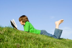 Boy Reading Outside In The Grass